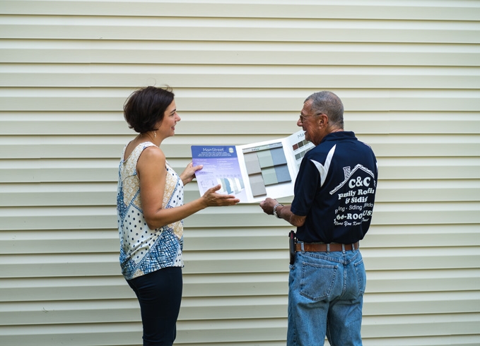 A roofer and a customer talking outside of a house.