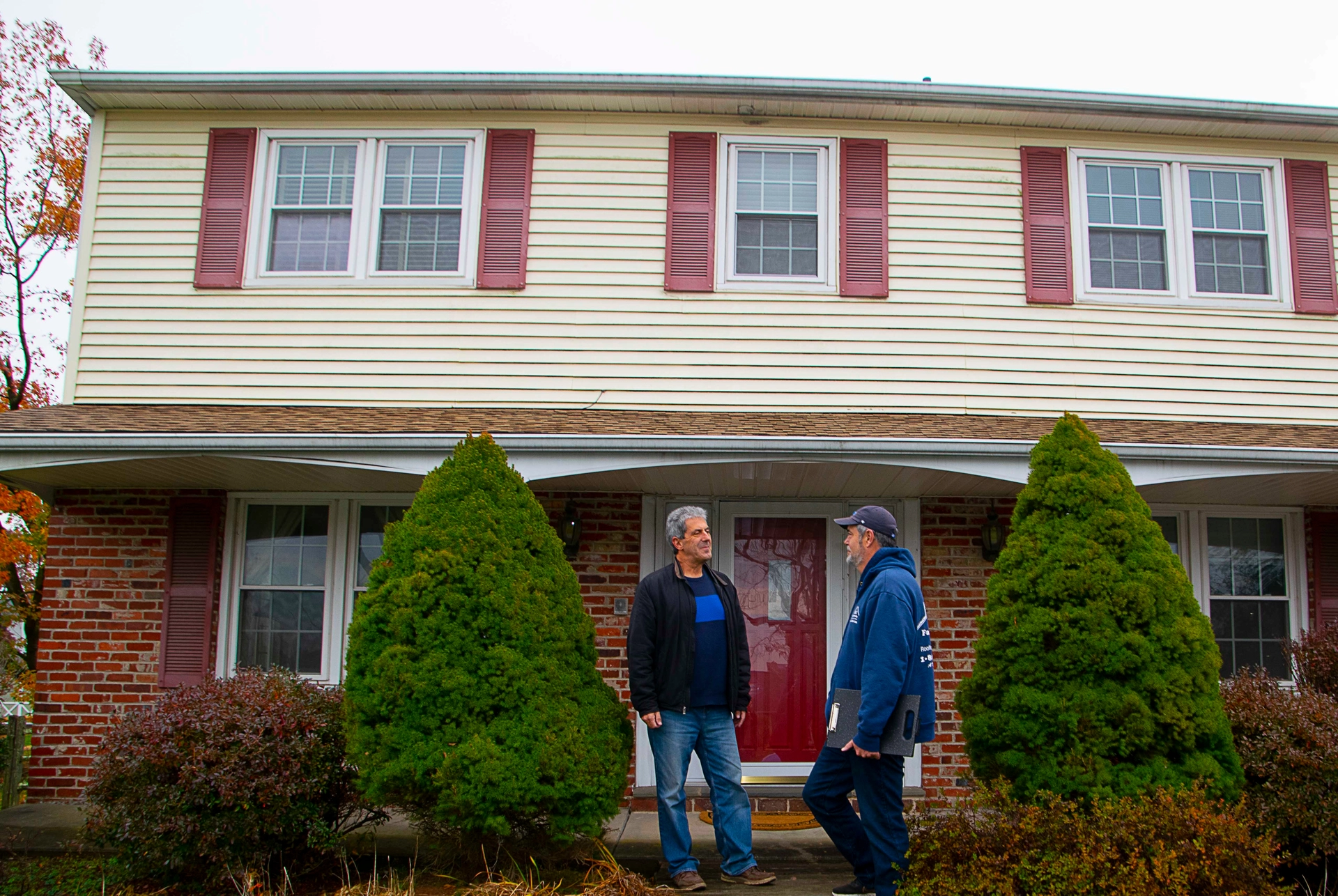 A roofer and a customer talking outside of a house.